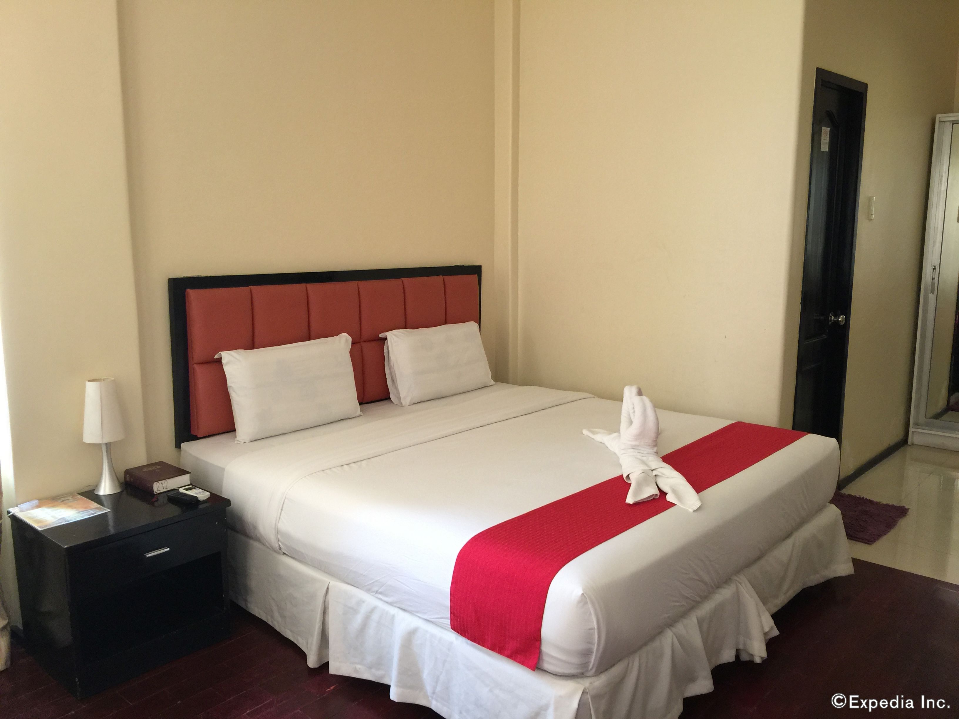 A hotel room with a bed, a nightstand, a lamp, and a door.