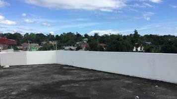 Una azotea con un muro blanco y un suelo de hormigón. Se ven casas y árboles al fondo.