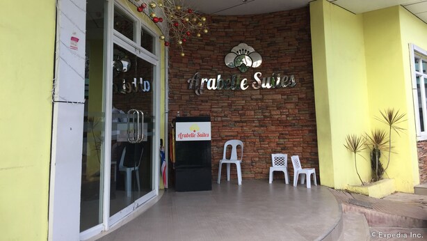 A hotel entrance with a brick facade, a sign reading "Arabelle Suites", and a few white plastic chairs outside. - Arabelle Suites (Tagbilaran)