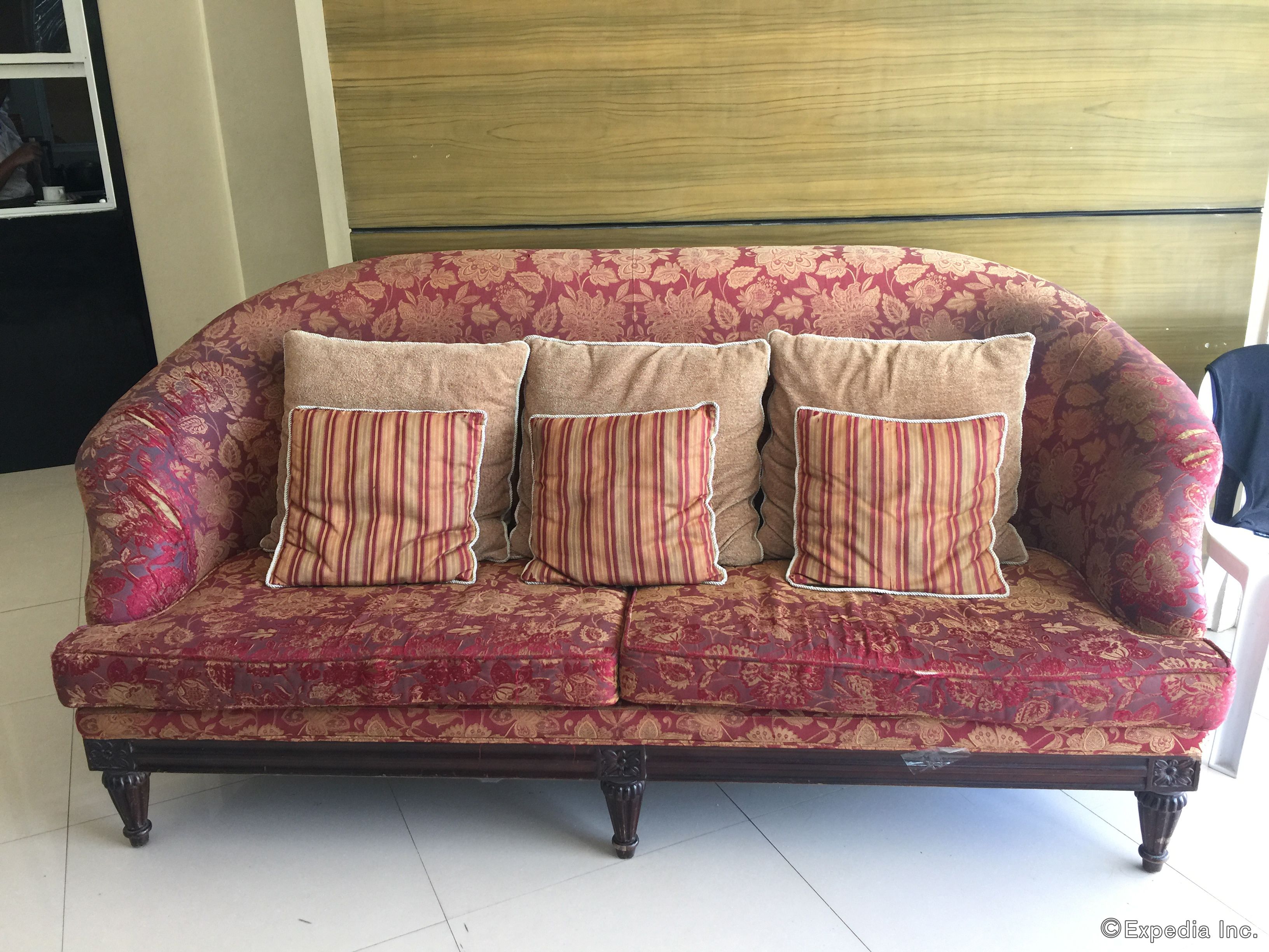 Un canapé recouvert d’un tissu à motifs floraux, agrémenté de coussins à rayures, dans une pièce dont un mur est recouvert de panneaux de bois.