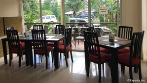 A restaurant with a sliding door, tables with chairs, and a view of parked cars and greenery outside. - Arabelle Suites (Tagbilaran)