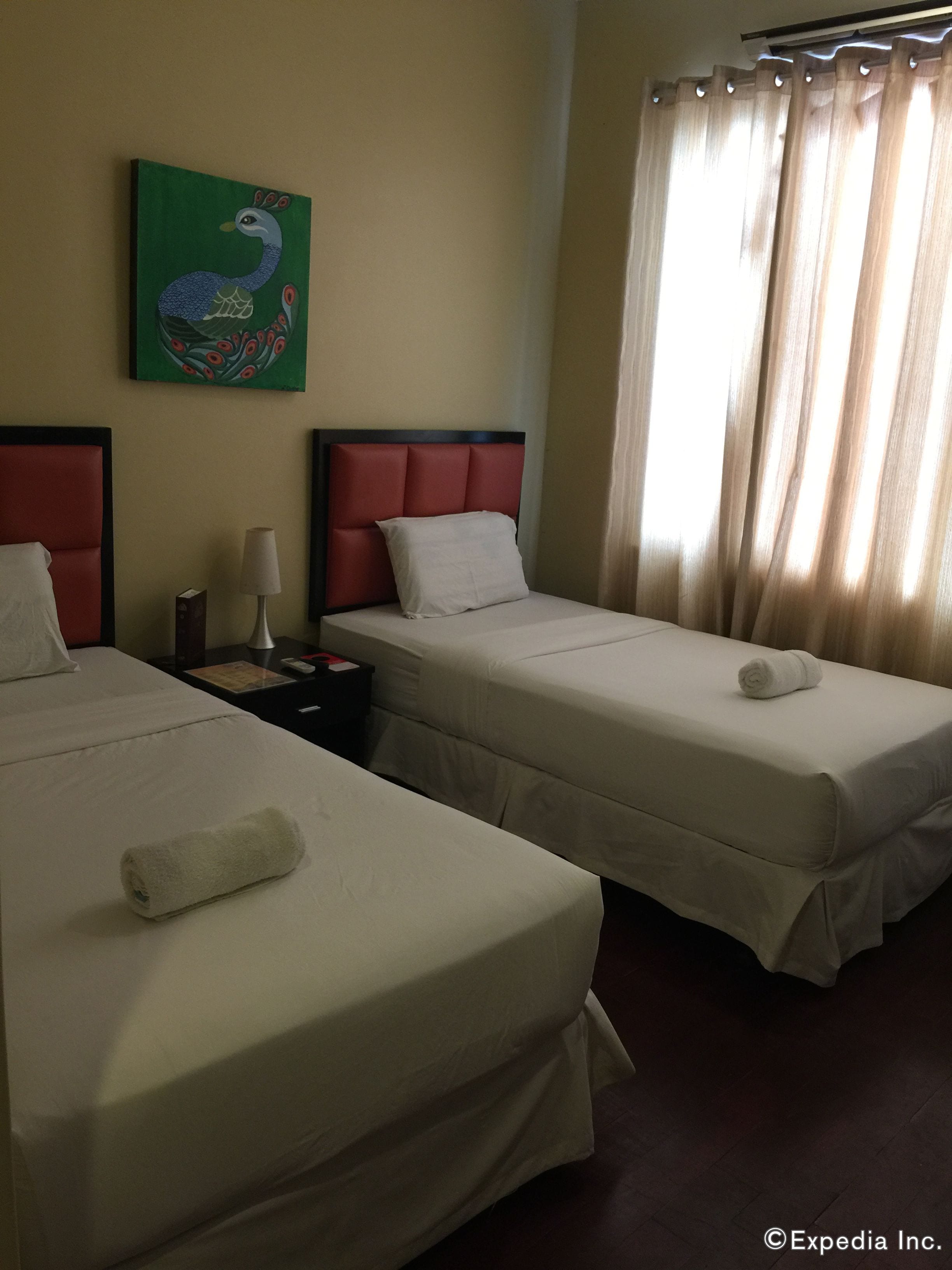 Habitación de hotel con dos camas, una mesita de noche, una lámpara, un cuadro y una ventana con cortinas.