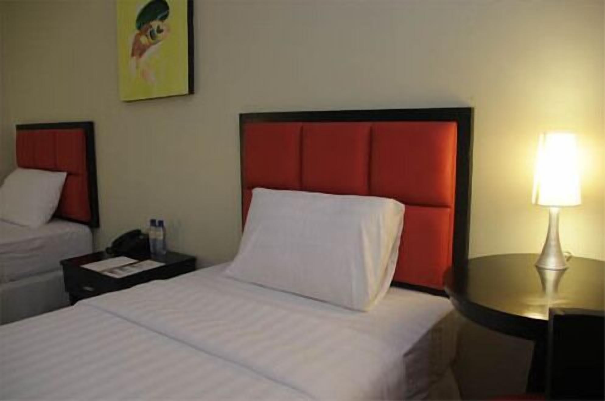 A hotel room with a bed, a nightstand, a lamp, and a painting on the wall.