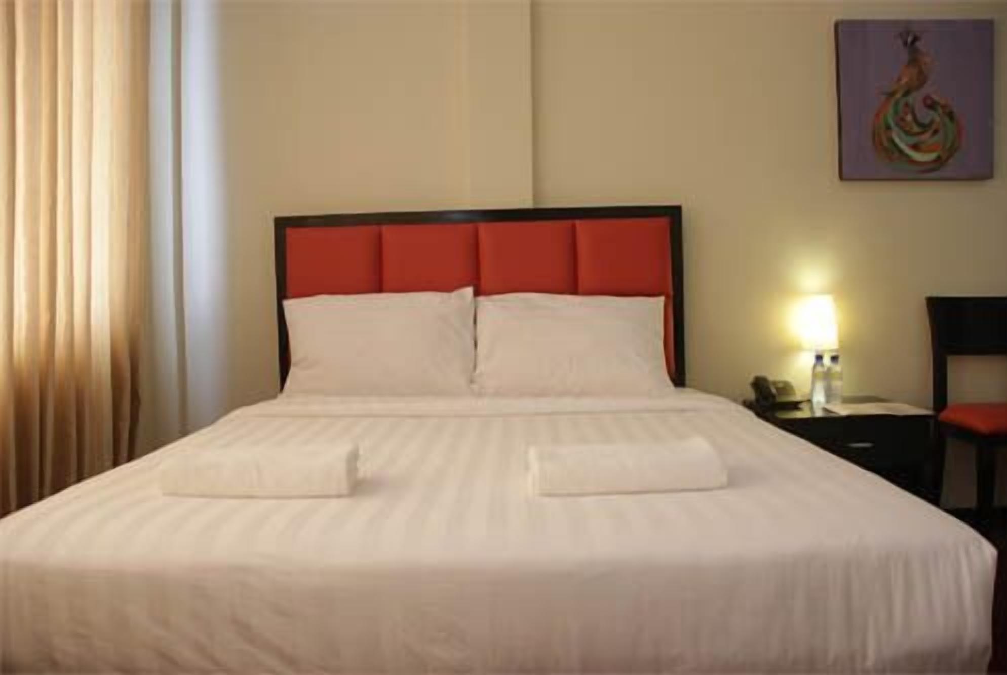 A hotel room with a large bed, a nightstand, a lamp, and a painting on the wall.