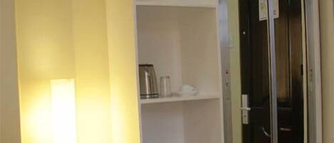 Una habitación con un armario blanco, un pequeño calentador y un ventanal de vidrio que da a otra estancia.