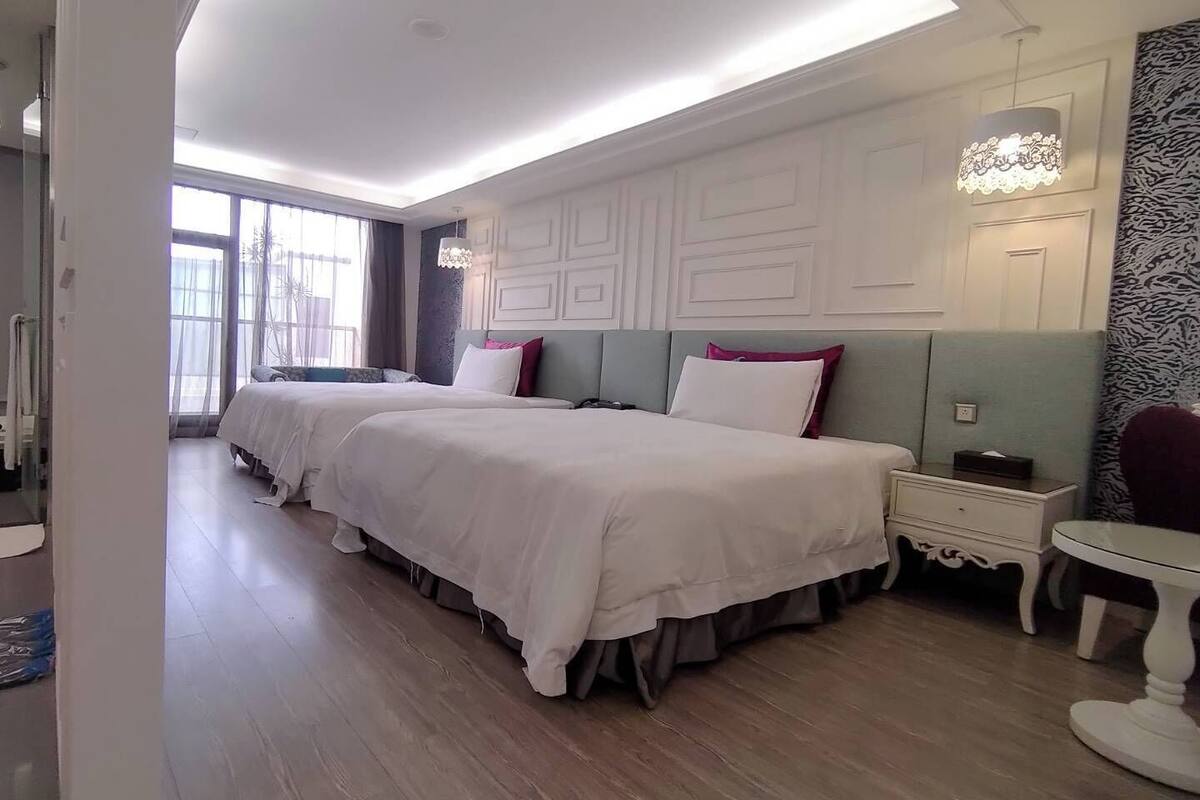 Une chambre d’hôtel avec deux lits, une petite table, une table de chevet et une grande fenêtre.