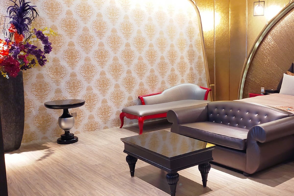 Une chambre à coucher moderne avec une tête de lit incurvée, un canapé, une table de chevet et un vase décoratif.