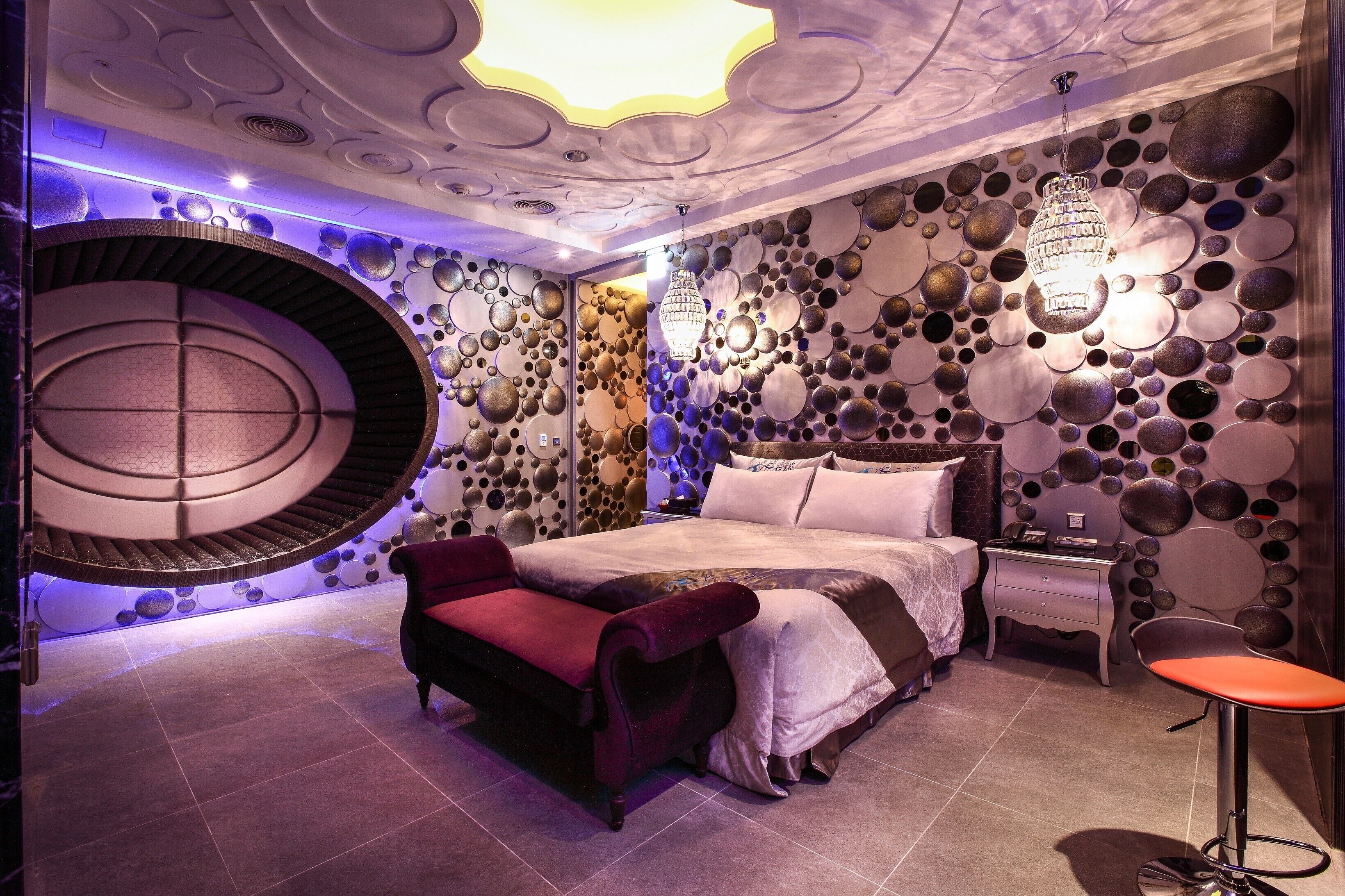 Un dormitorio moderno con un diseño de pared circular, una cama, una silla roja y una mesita.