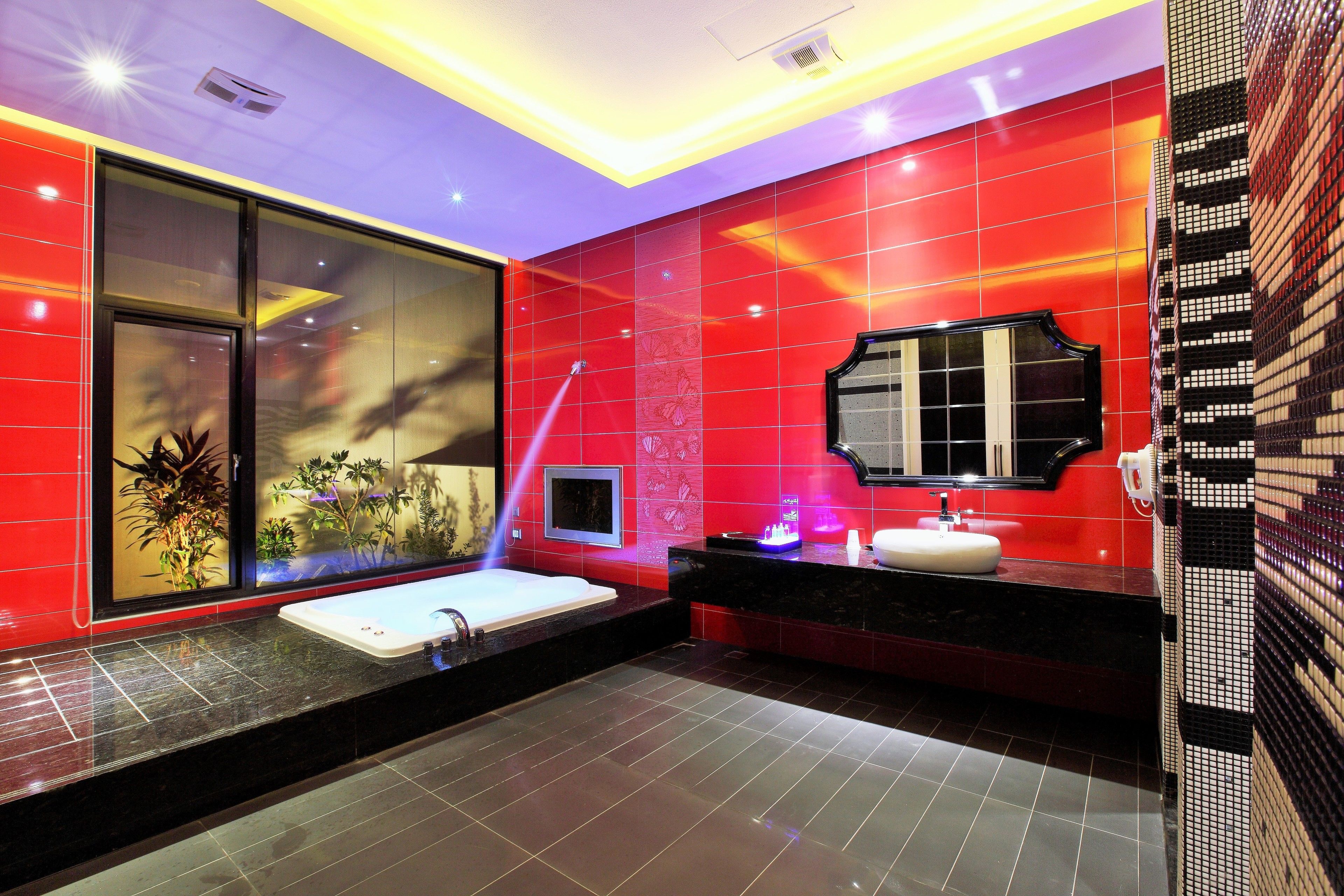 A modern bathroom with a large bathtub, a vanity with a mirror, and a window with a view of plants.
