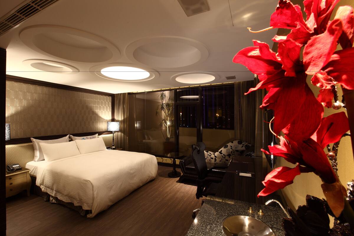 Une chambre d’hôtel avec un grand lit, un bureau, une chaise, une table de chevet, une lampe, un miroir et une fenêtre donnant sur le paysage nocturne.
