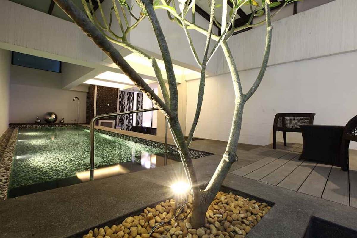 Un espace piscine intérieure agrémenté d’un arbre, de sièges et d’une petite cascade.
