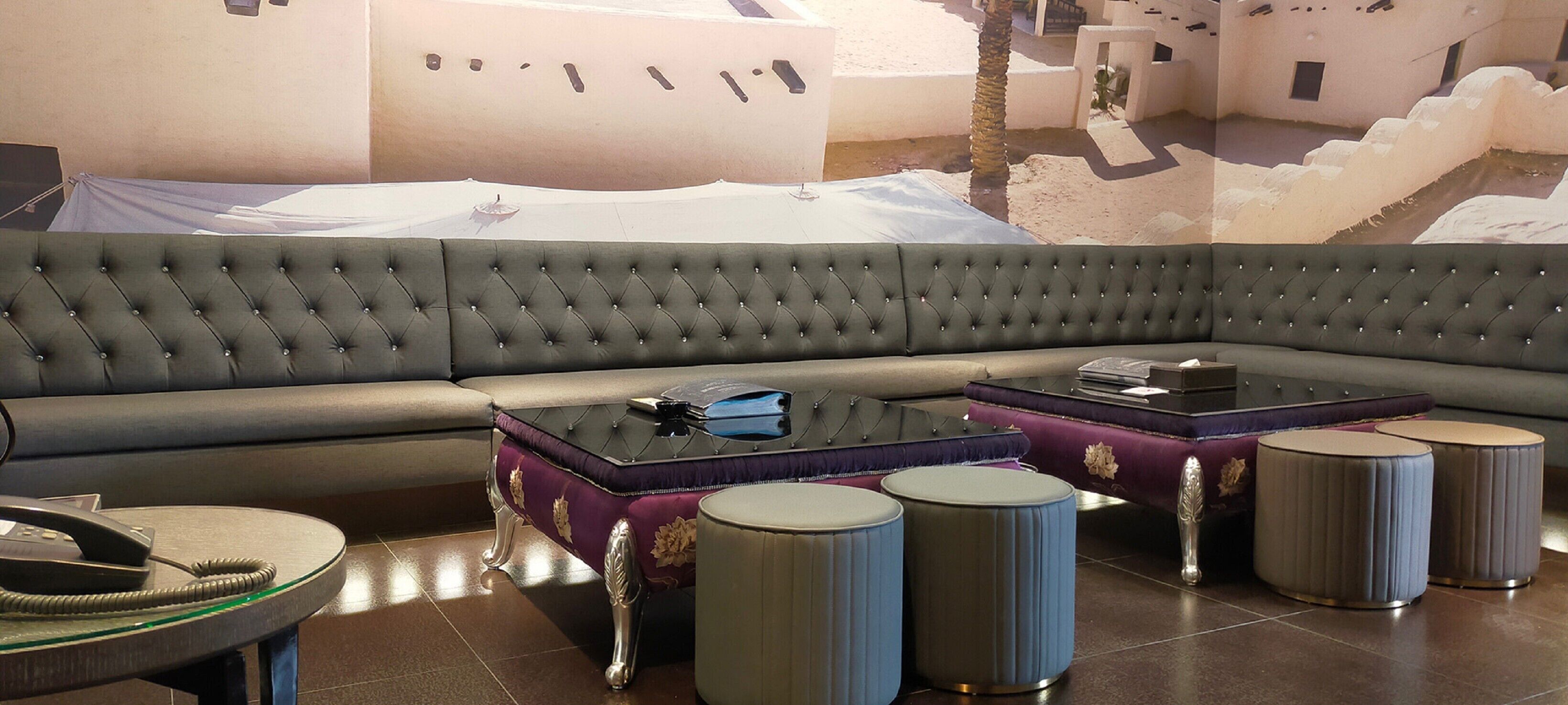 Een moderne loungehoek met een royale hoekbank, een zwarte gestoffeerde salontafel en drie ronde voetenbankjes.
