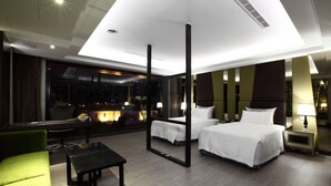 Una habitación de hotel moderna con una cama grande, un sofá verde, una mesita y vistas a la ciudad a través de amplios ventanales.