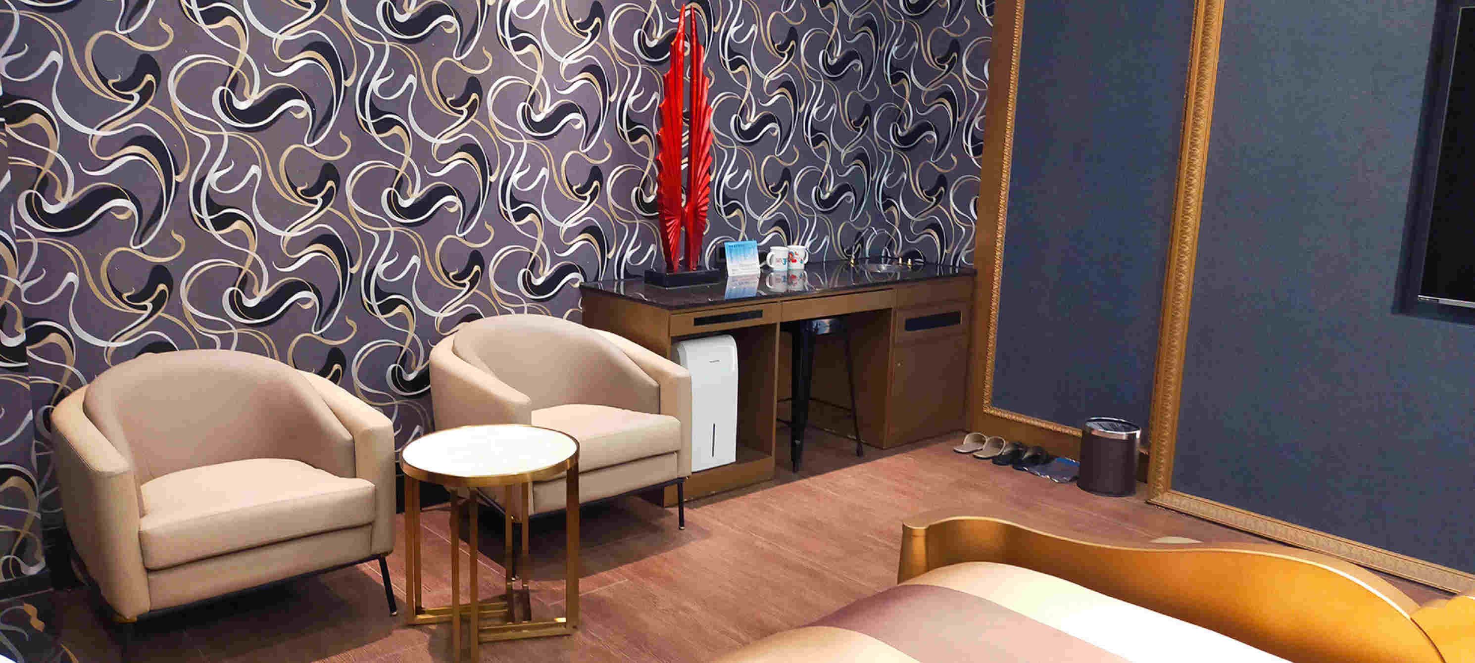 A hotel room with a patterned wallpaper, a desk with a mirror, a bed, two armchairs, and a small round table.
