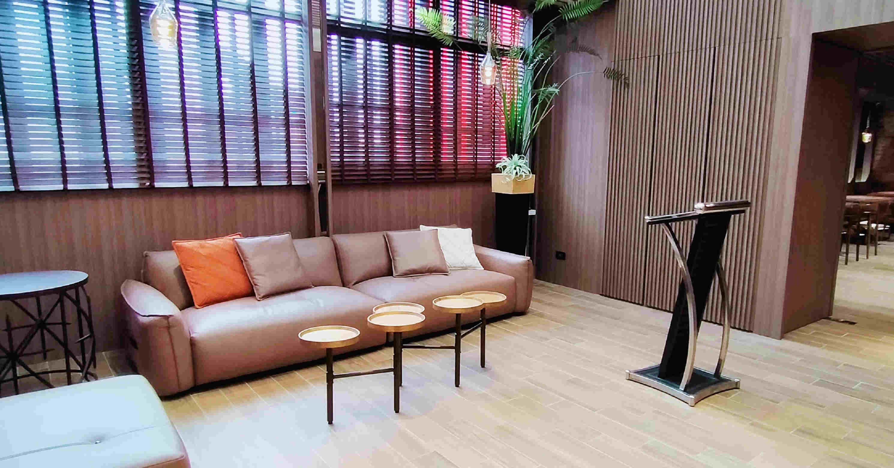 Een moderne zithoek met een leren bank, ronde tafels en een hoge vloerlamp.