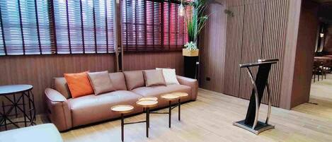 Een moderne zithoek met een leren bank, ronde tafels en een hoge vloerlamp.