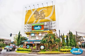 A building with a large yellow sign featuring a lion, a smaller sign with 'FUN-D' and a phone number, and a coffee shop entrance with 'Coffee & Restaurant' signage. - FUN-D Hostel Chiang rai (Chiang Rai)