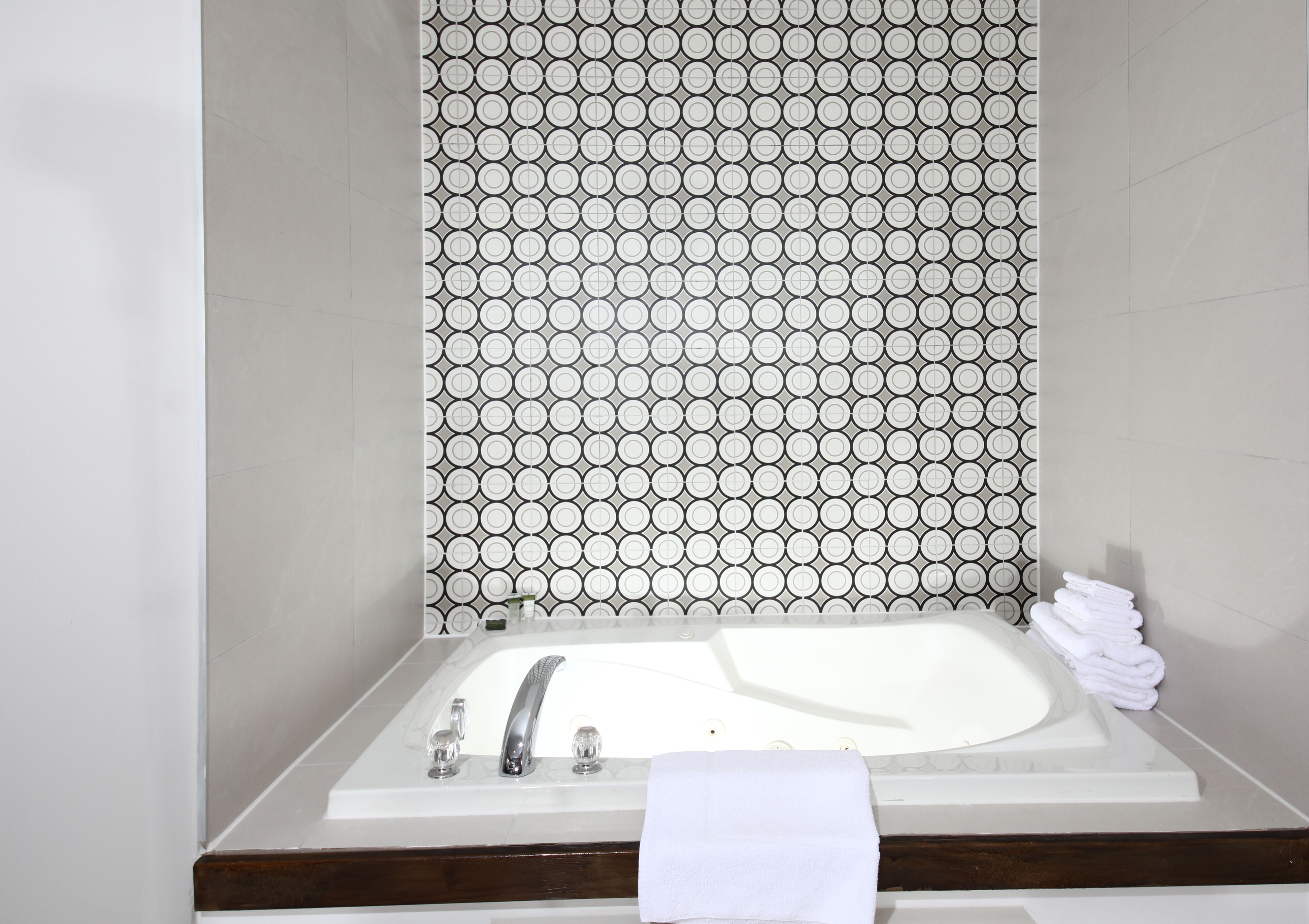 A bathroom with a white bathtub, a towel rack with towels, and a patterned wall.