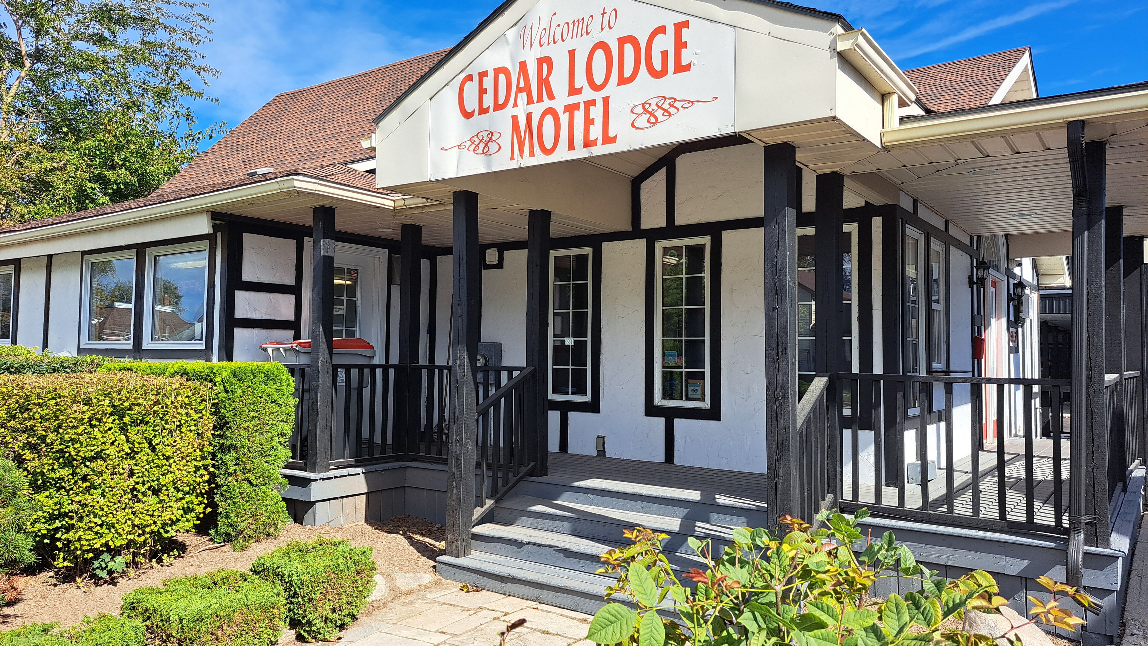 Een Cedar Lodge Motel met een witte gevel, zwarte accenten en een uitnodigend bord.