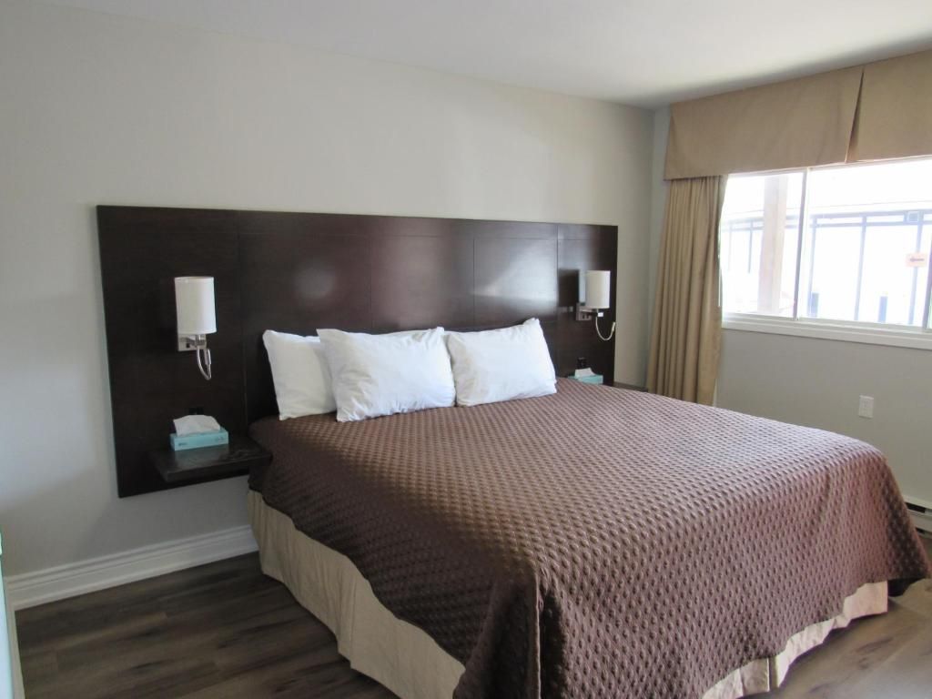 A hotel room with a large bed, two bedside tables, a headboard, and a window with curtains.