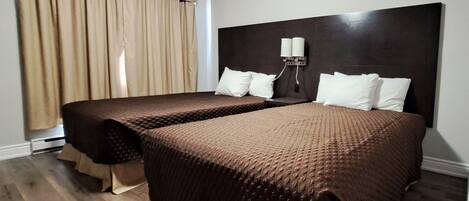 Habitación de hotel con dos camas, cabecera oscura, luz de pared y ventana con cortinas.
