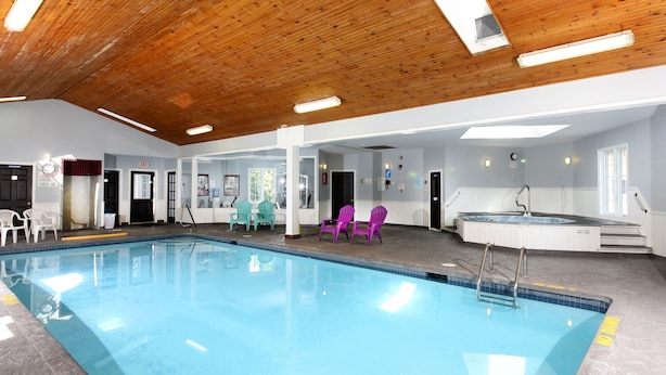 An indoor swimming pool with clear water, surrounded by white walls and a wooden ceiling. There are chairs and a hot tub area visible. - Cedar Lodge Motel (Goderich)