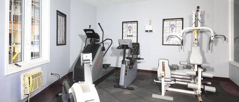 Sala de ginástica com equipamentos de exercício, incluindo esteira, elíptico e máquina de musculação.