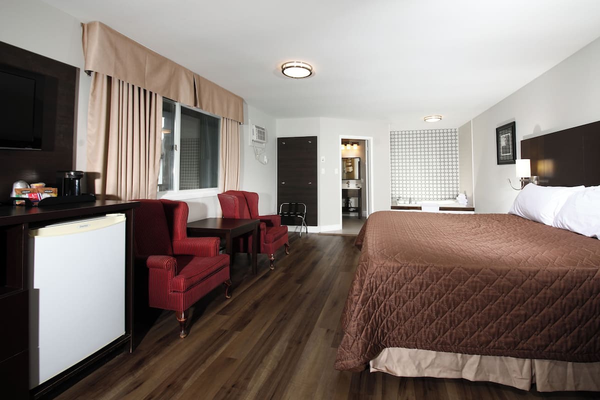 A hotel room with a bed, a desk, a chair, a small refrigerator, and a window with curtains.