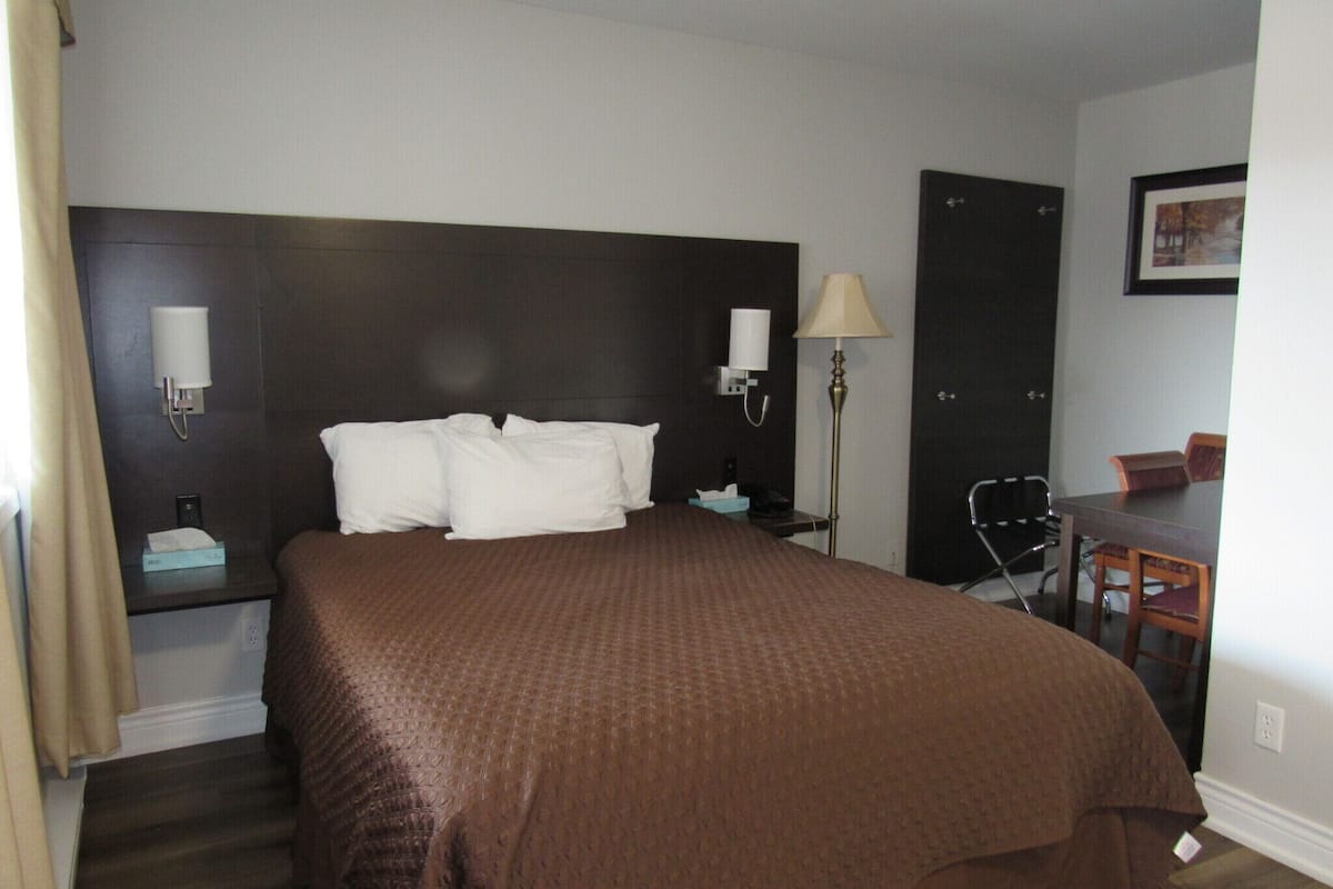 A hotel room with a large bed, two bedside lamps, a desk with a chair, and a door.