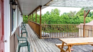 A covered wooden deck with a picnic table and chairs, a railing, and a view of greenery in the background. - Cedar Lodge Motel (Goderich)