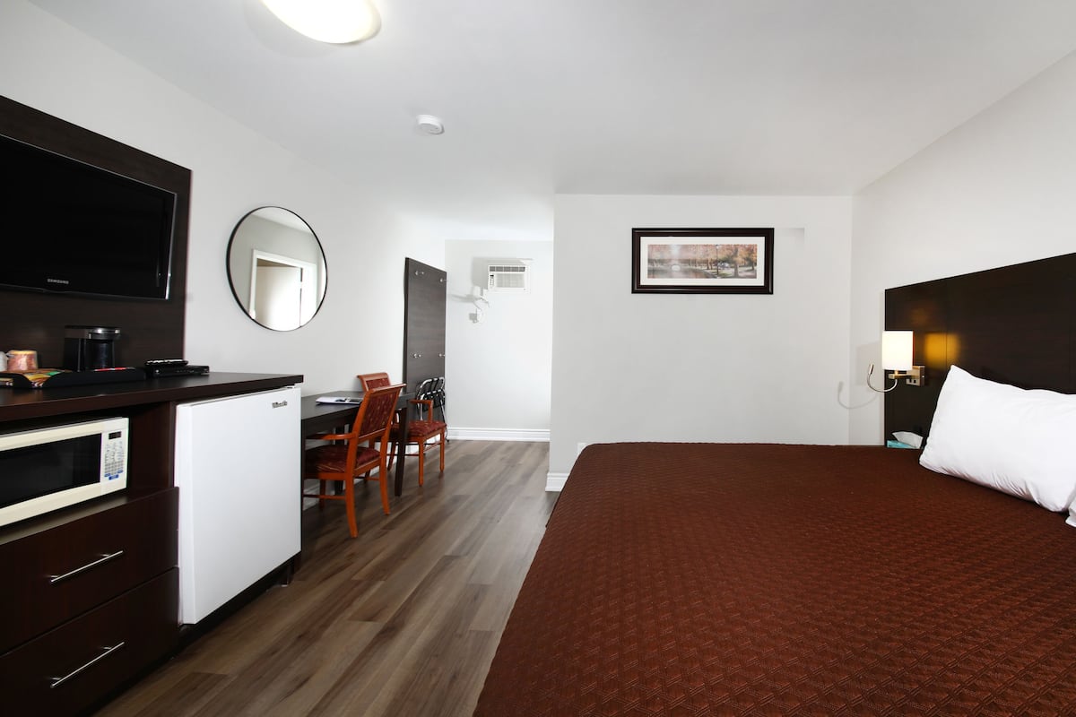 A hotel room with a bed, a desk with a computer, a chair, a TV, and a framed picture on the wall.