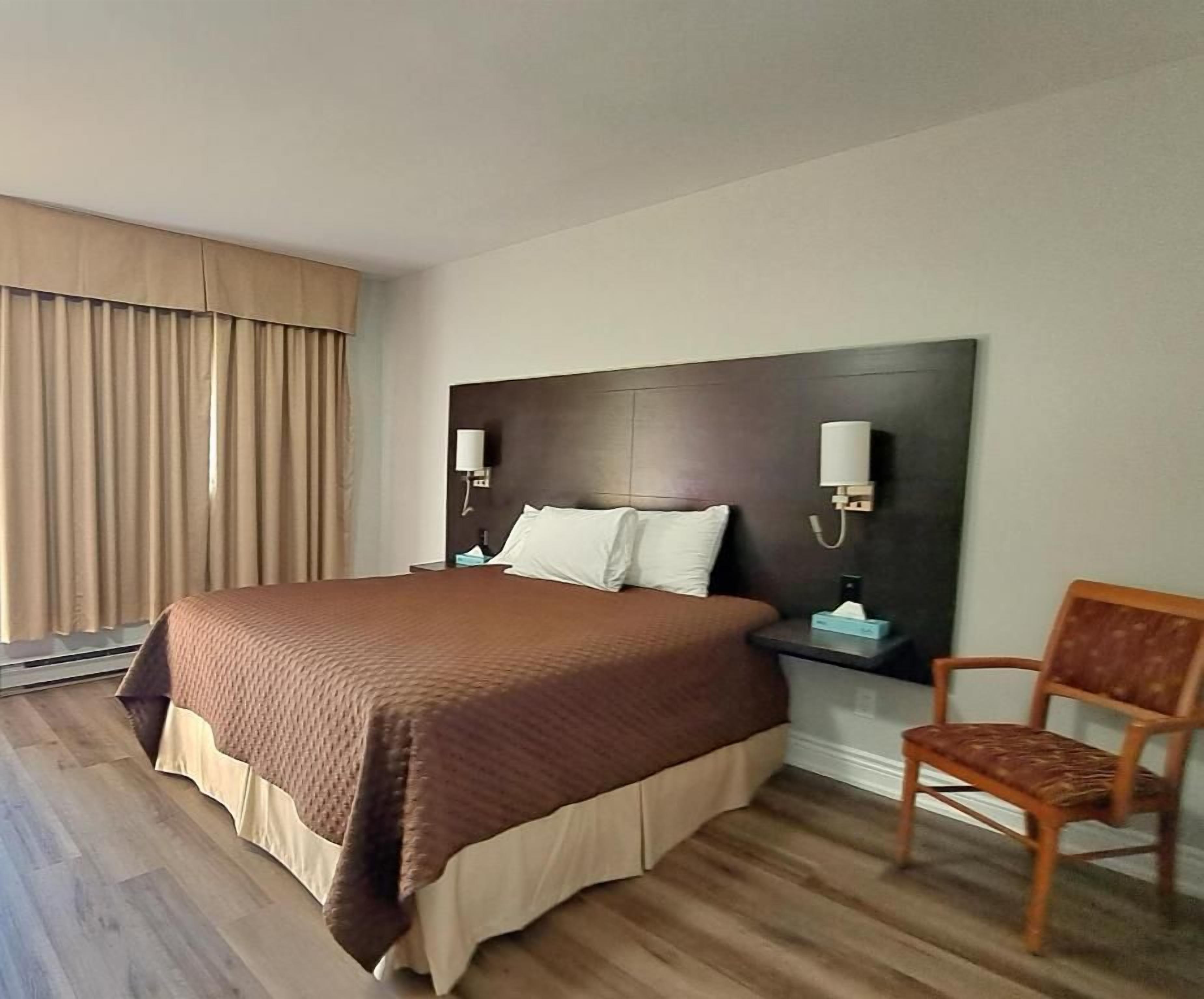 A hotel room with a large bed, a nightstand with lamps, a chair, and a view of the outdoors.