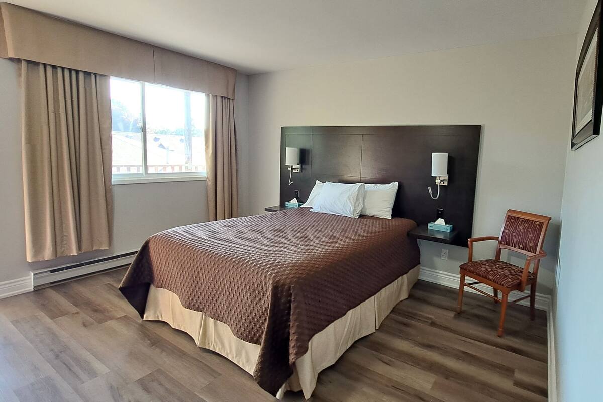 A hotel room with a large bed, a chair, a nightstand, a lamp, and a window with curtains.