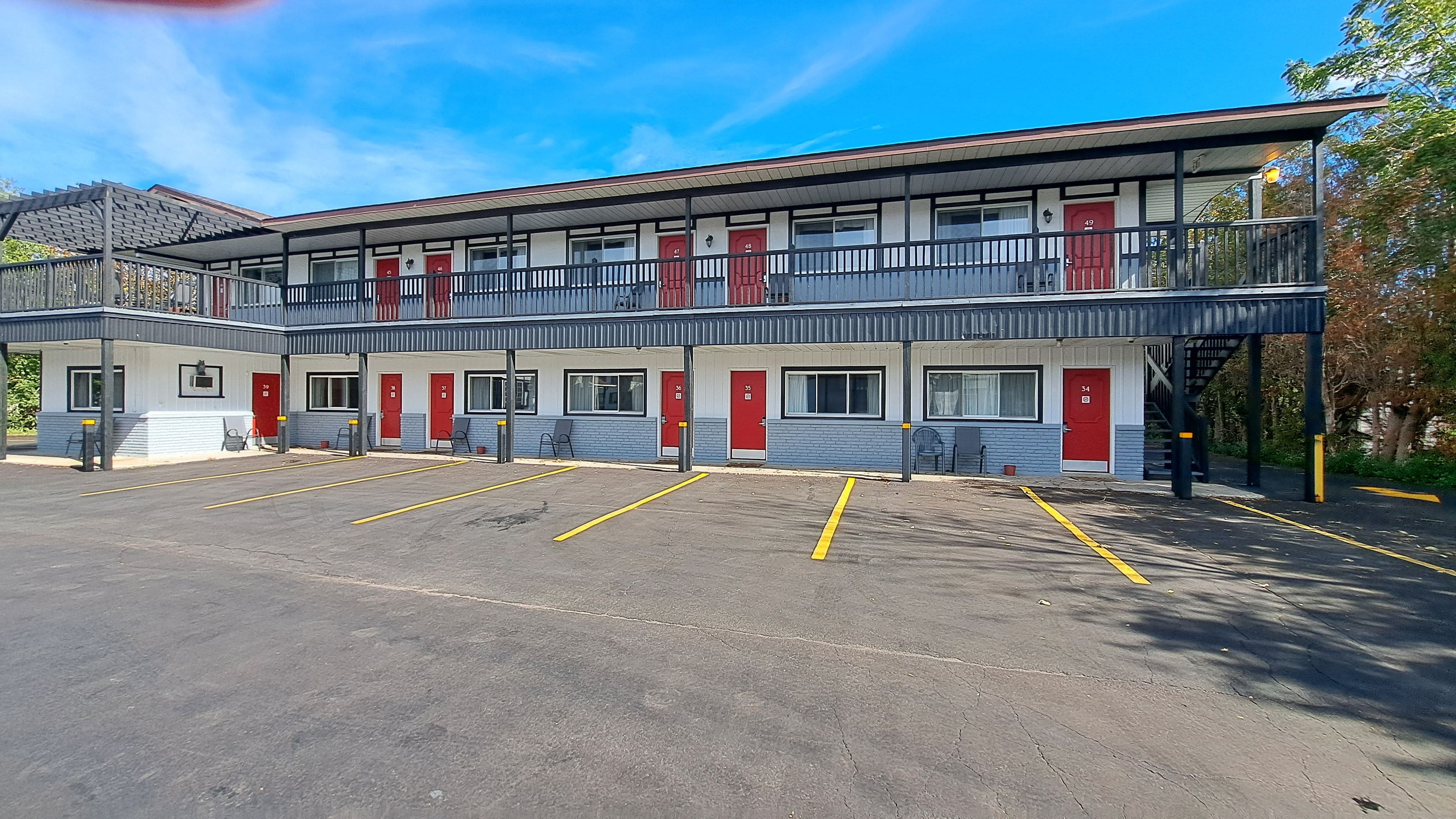 Un motel comprenant plusieurs chambres, un parking couvert et un escalier menant à un étage supérieur.