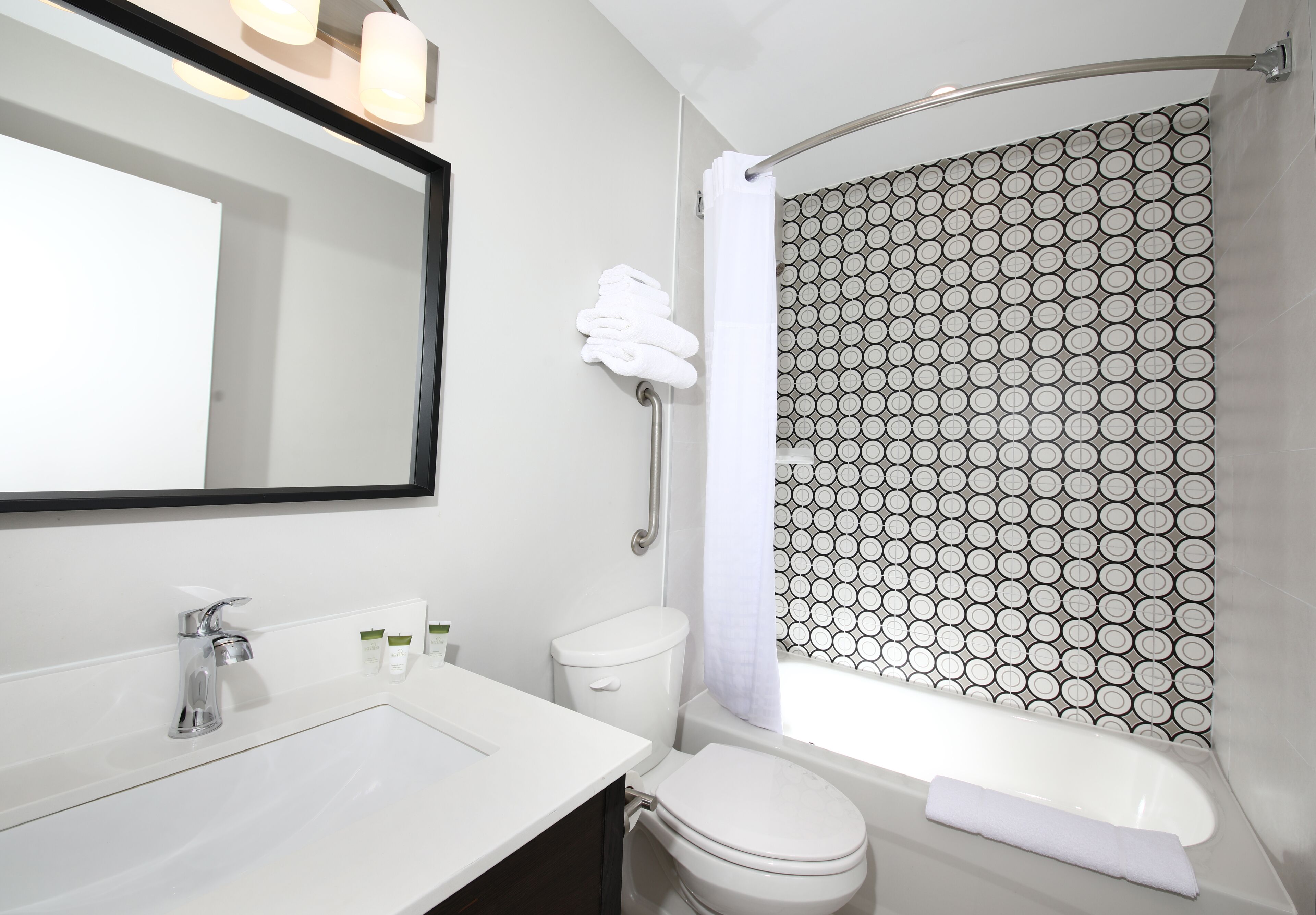 Une salle de bain moderne avec un lavabo blanc, un miroir, des toilettes et une baignoire.