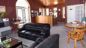 A cozy room with a leather sofa, a wooden table with chairs, a reception desk, and a large arched window. - Cedar Lodge Motel (Goderich)
