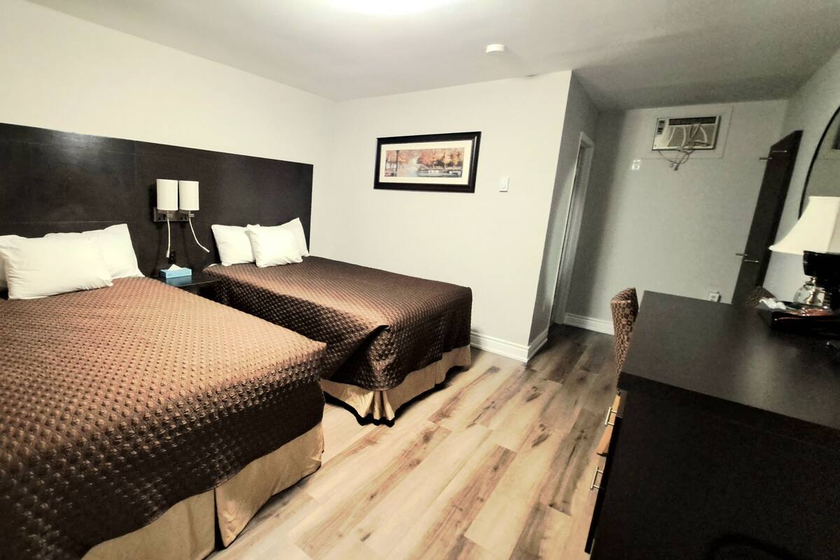 A hotel room with two beds, a desk, a chair, and a framed picture on the wall.