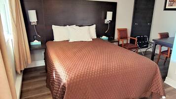 A hotel room with a large bed, a desk, a chair, and a door.