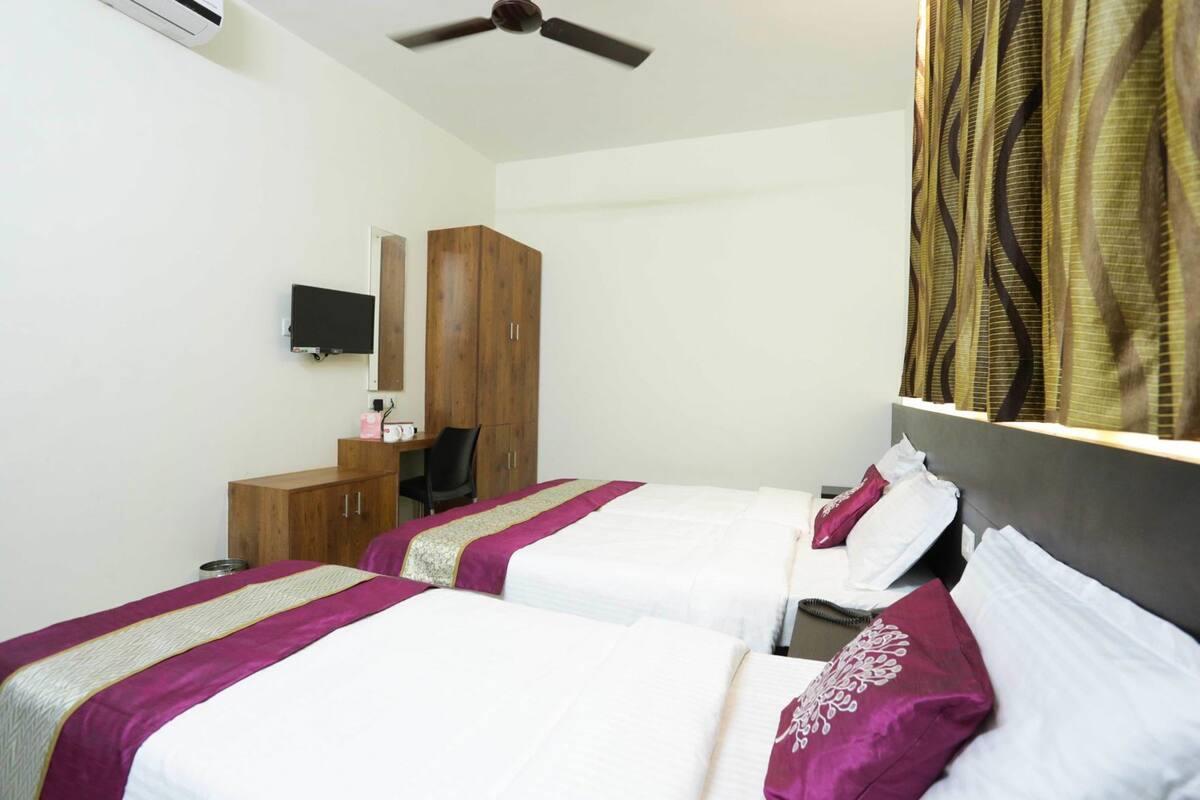 Een hotelkamer met twee bedden, een bureau, een stoel, een televisie en een plafondventilator.
