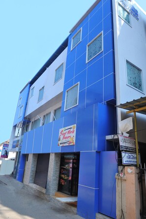 Un edificio con fachada azul y blanca, un letrero que dice 'Sweet World Bakers' y un toldo cerrado a nivel de calle.