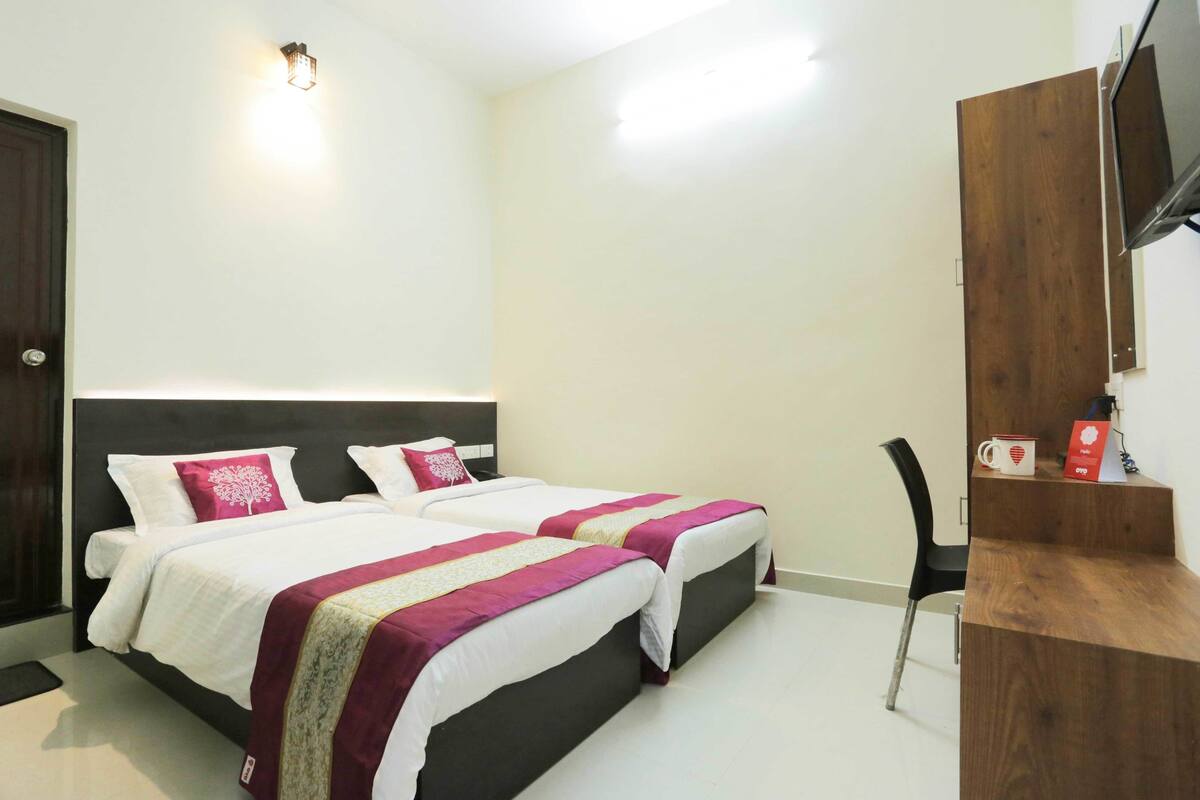 Een hotelkamer met twee bedden, een houten bureau, een stoel en een aan de muur bevestigde televisie.