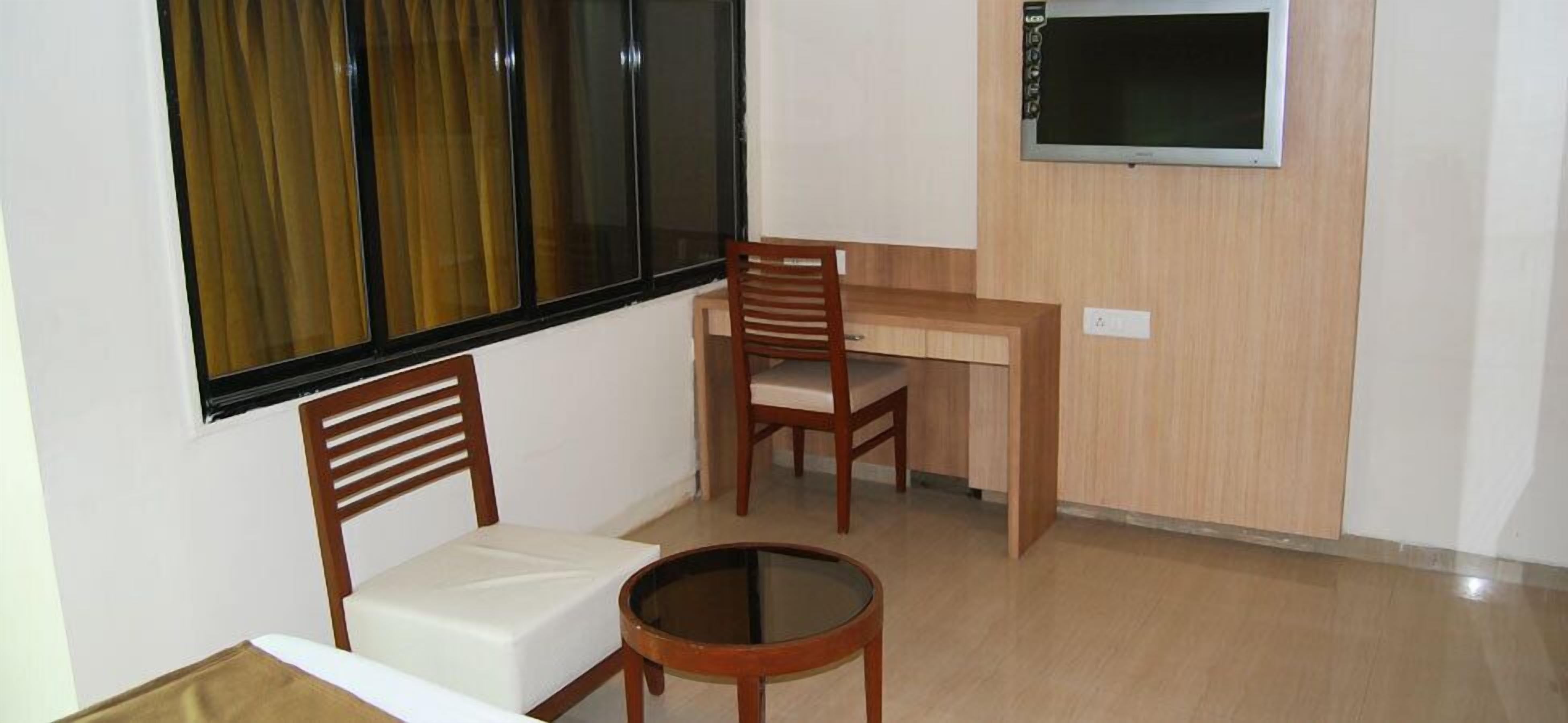 Une petite pièce comprenant un bureau, deux chaises, une table ronde et un téléviseur fixé au mur.
