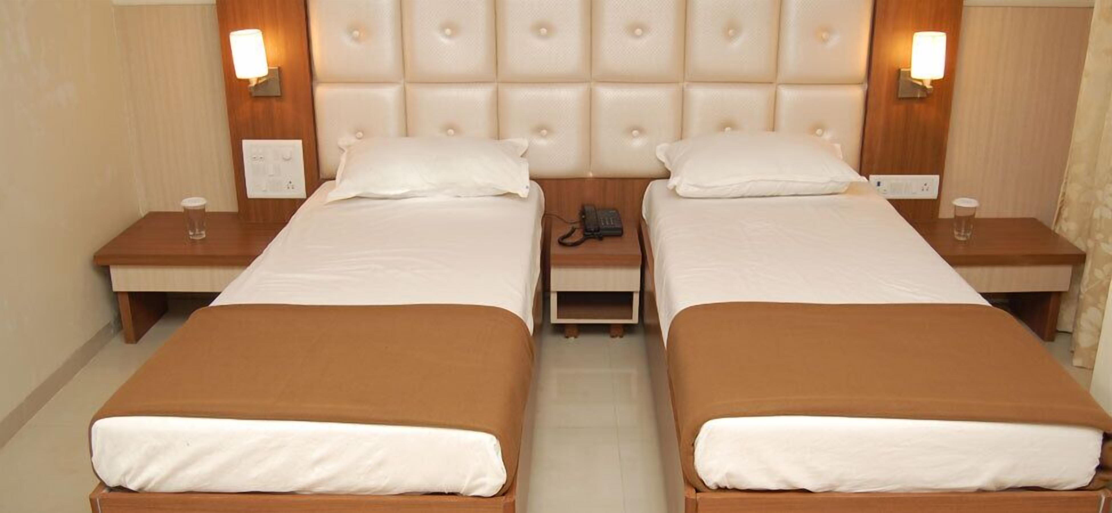 A hotel room with two single beds, a padded headboard, bedside lamps, and a telephone on the nightstand.