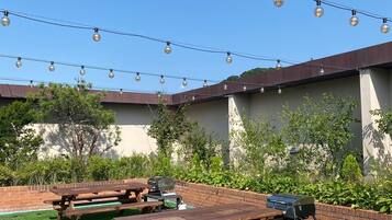 An outdoor patio area with picnic tables, string lights, and a barbecue grill.