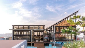 A modern building with a glass facade, a BBQ zone, and a wooden deck area. - Benikea The Bliss Hotel (Incheon)