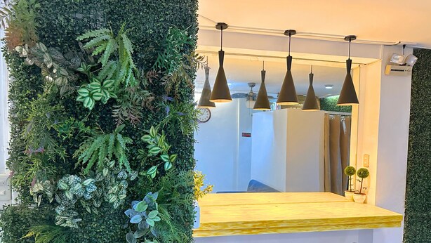 Una zona de bar con un jardín vertical verde, una barra de madera y tres taburetes.