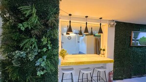 Cocina moderna con encimera de madera, taburetes de bar, luces colgantes y una pared verde con follaje.