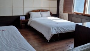 Una habitación de hotel con dos camas, piso de madera, un ventanal grande con persianas y un diseño circular en el techo.
