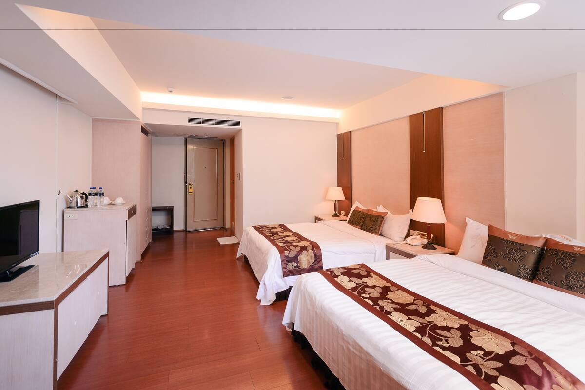 A hotel room with two beds, a desk, a television, and a bathroom.