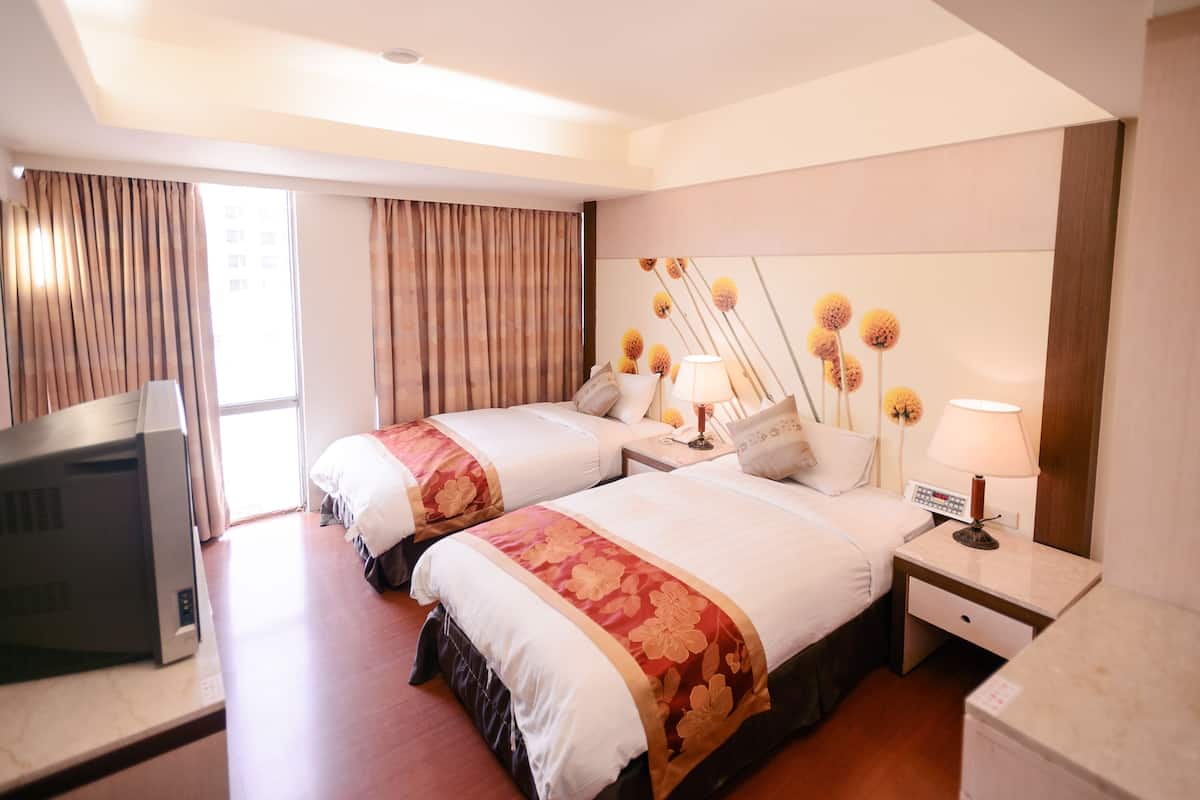 A hotel room with two beds, a TV, a desk, and a lamp.